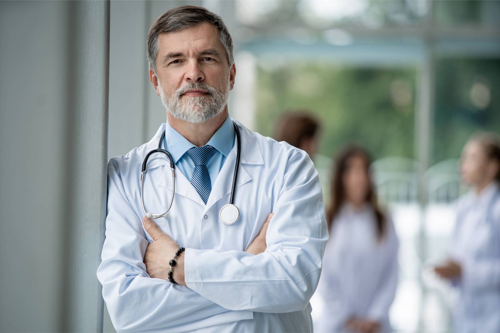 Portrait of a senior male doctor leaning against a wall with his arms folded
