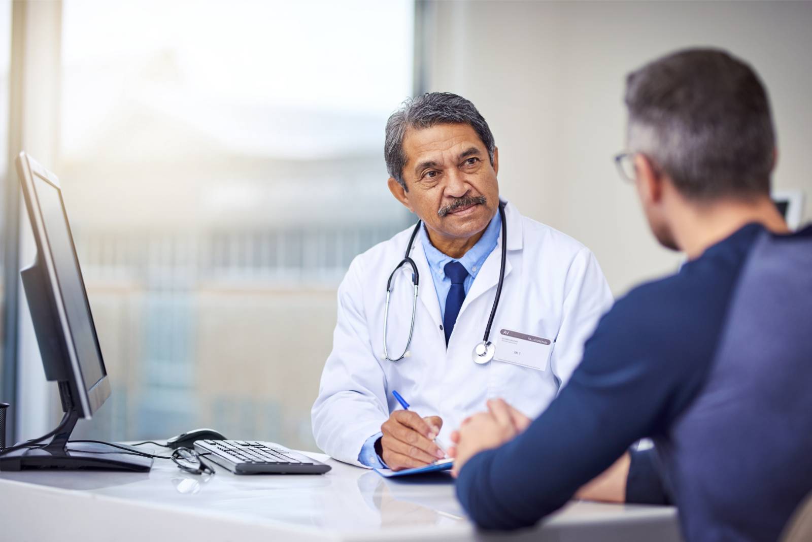 A senior male doctor listening to a middle-aged male patient's concerns